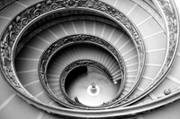 This is a black and white photograph of the ornate stairway at the Vatican Museum.