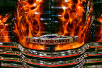 Color photograph of the hood of a Chevrolet set afire with flames